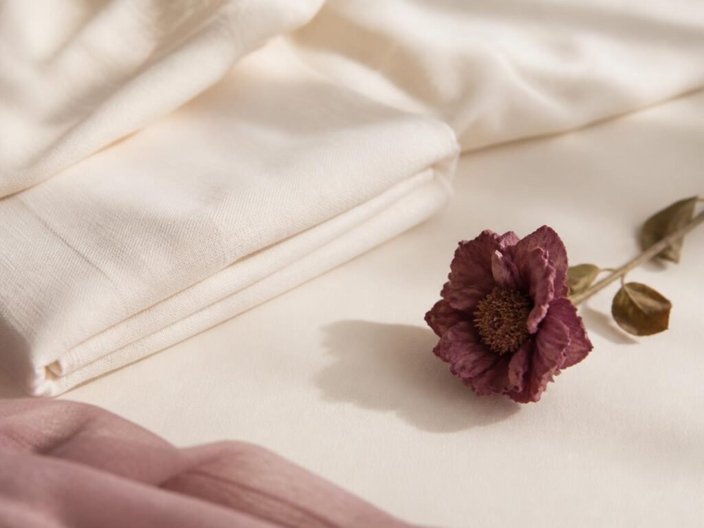 A single plum-toned flower resting on soft cream fabric